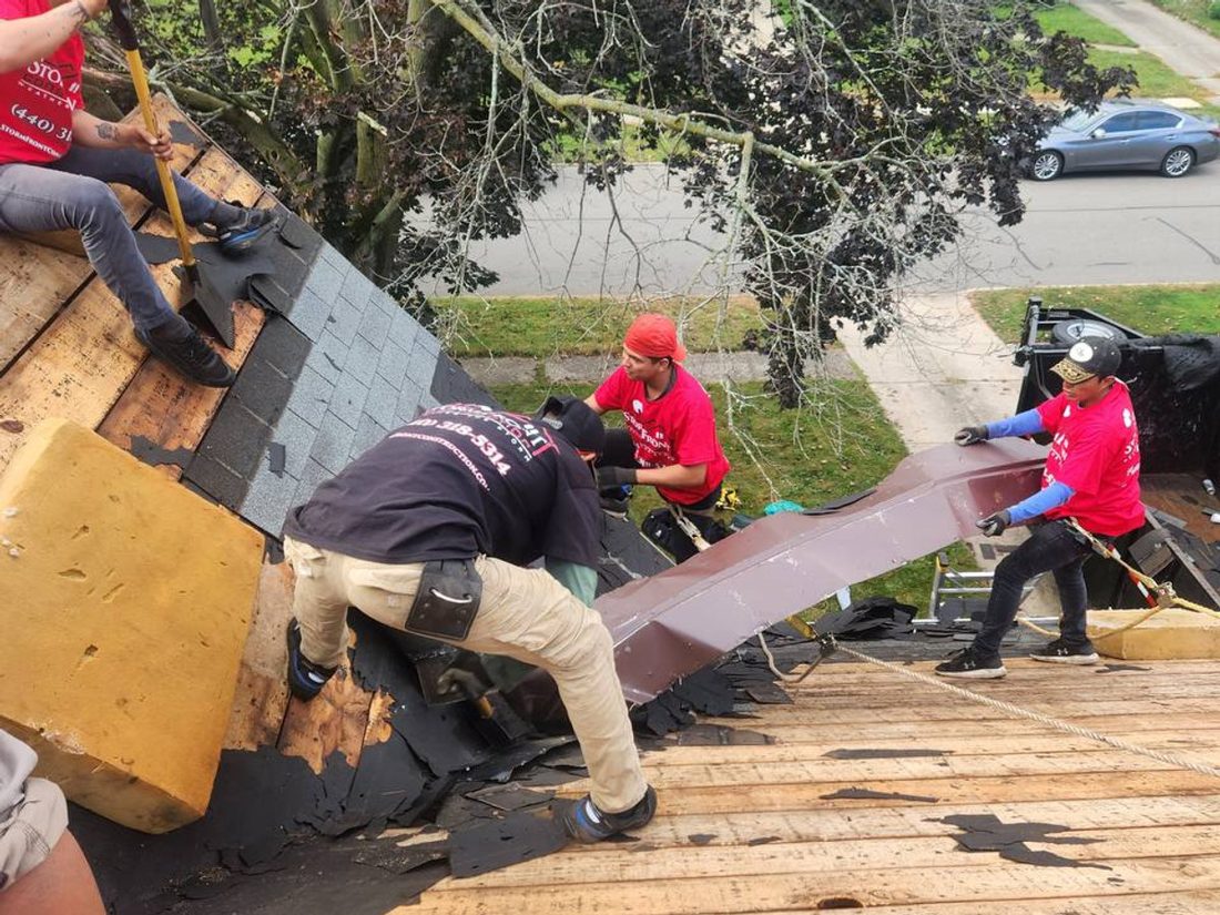 Stormfront crew in red shirts tearing old shingles off down to the wood deck