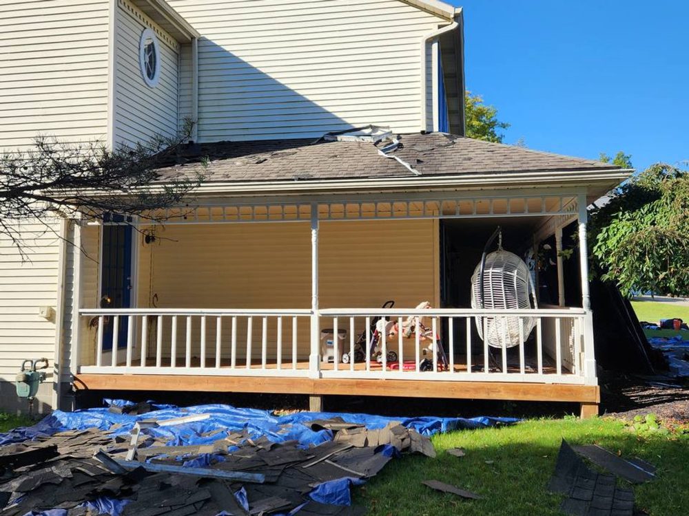 Blue tarps on the lawn holding torn-off shingles beside a damaged porch roof