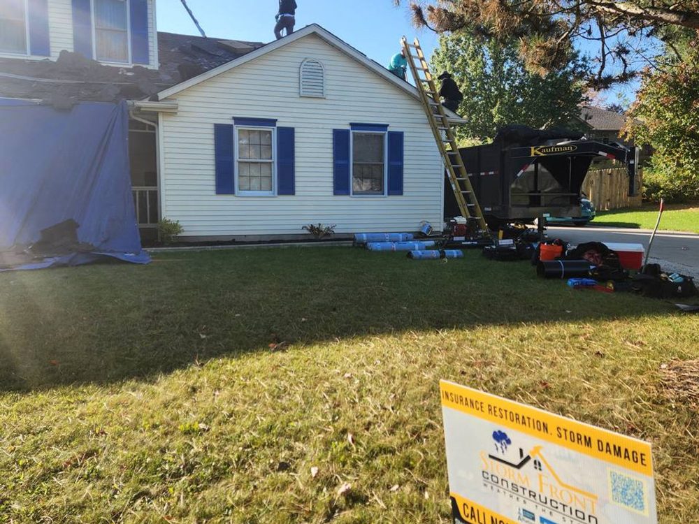 Stormfront job site: a tarp over the side of a white house, a trailer in the drive, and a Stormfront insurance-restoration sign in the yard