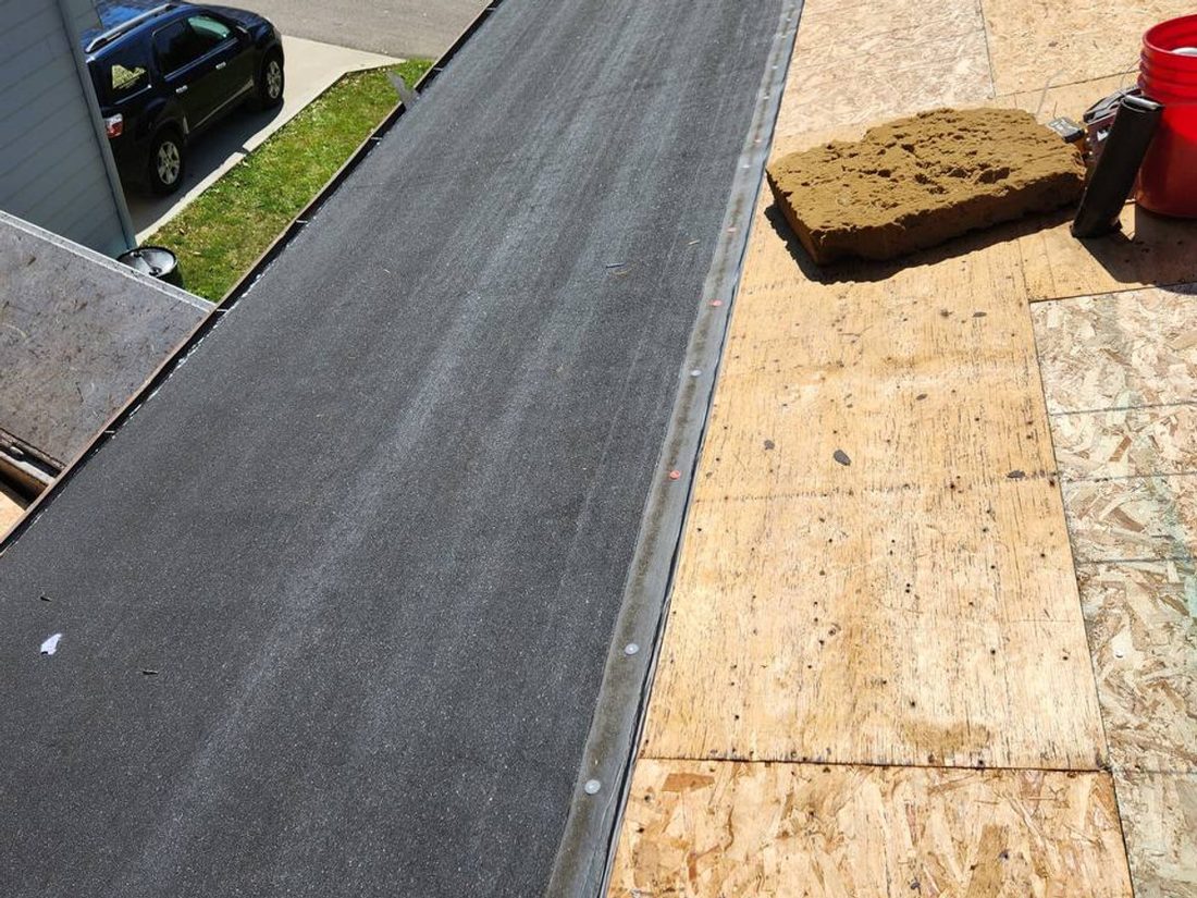 Black underlayment laid along the roof edge, with bare wood decking beside it